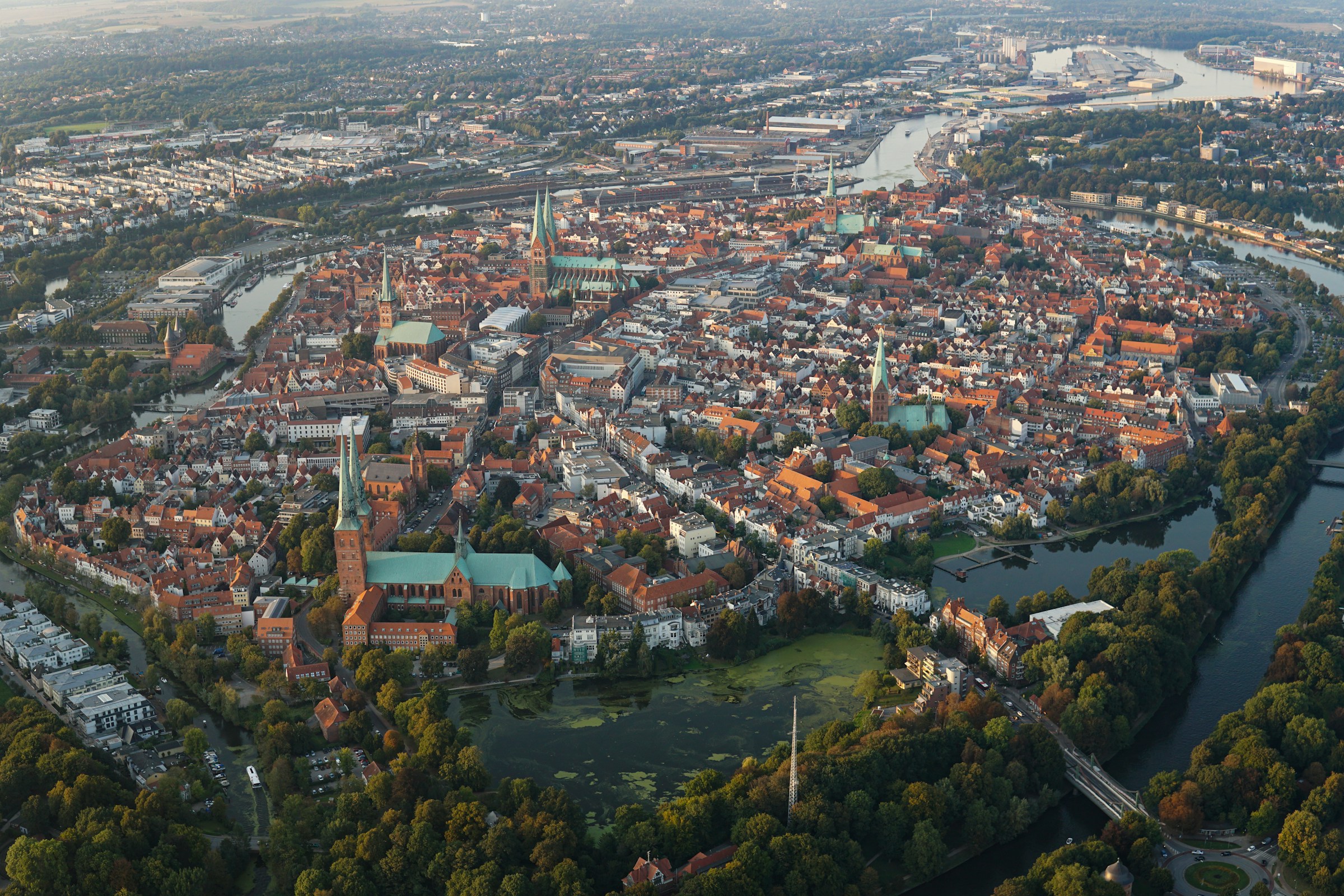 Ein Leuchtturm aus braunen Ziegeln in mitten einer grünen Landschaft mit einem Hochhaus im Hintergrund.